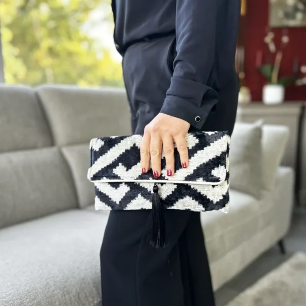 Du noir, de l’écru et un graphisme qui attire immédiatement le regard. 🖤 Cette pochette Ikat noire femme est confectionnée en velours 100 % soie pour un toucher doux et une allure résolument chic. Son motif artisanal rend chaque pièce unique. Sa fermeture magnétique garde vos essentiels à portée de main, tandis que son pompon noir en soie apporte la petite touche sophistiquée qui change tout.